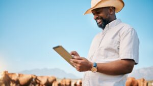 Agricultor negro sosteniendo su tablet frente a su ganado.