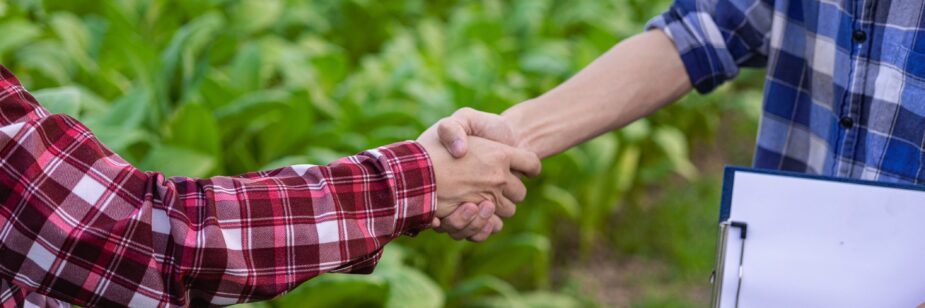 Dos hombres dándose la mano detrás de una plantación agrícola.