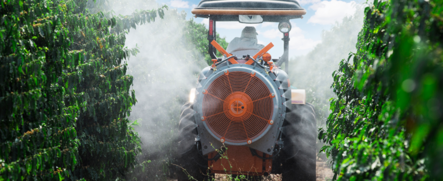 Pulverización en el café con equipo asistido por aire acoplado a un tractor entre hileras de cafetos.